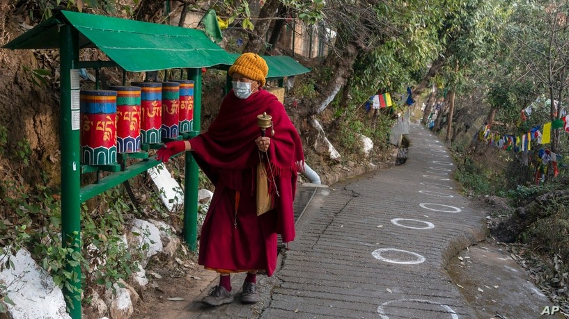 An exile Tibetan Buddhist monk rotates prayer wheels next to a path marked with circles for voters to ensure social distancing in Dharmsala, India. (AP Photo)